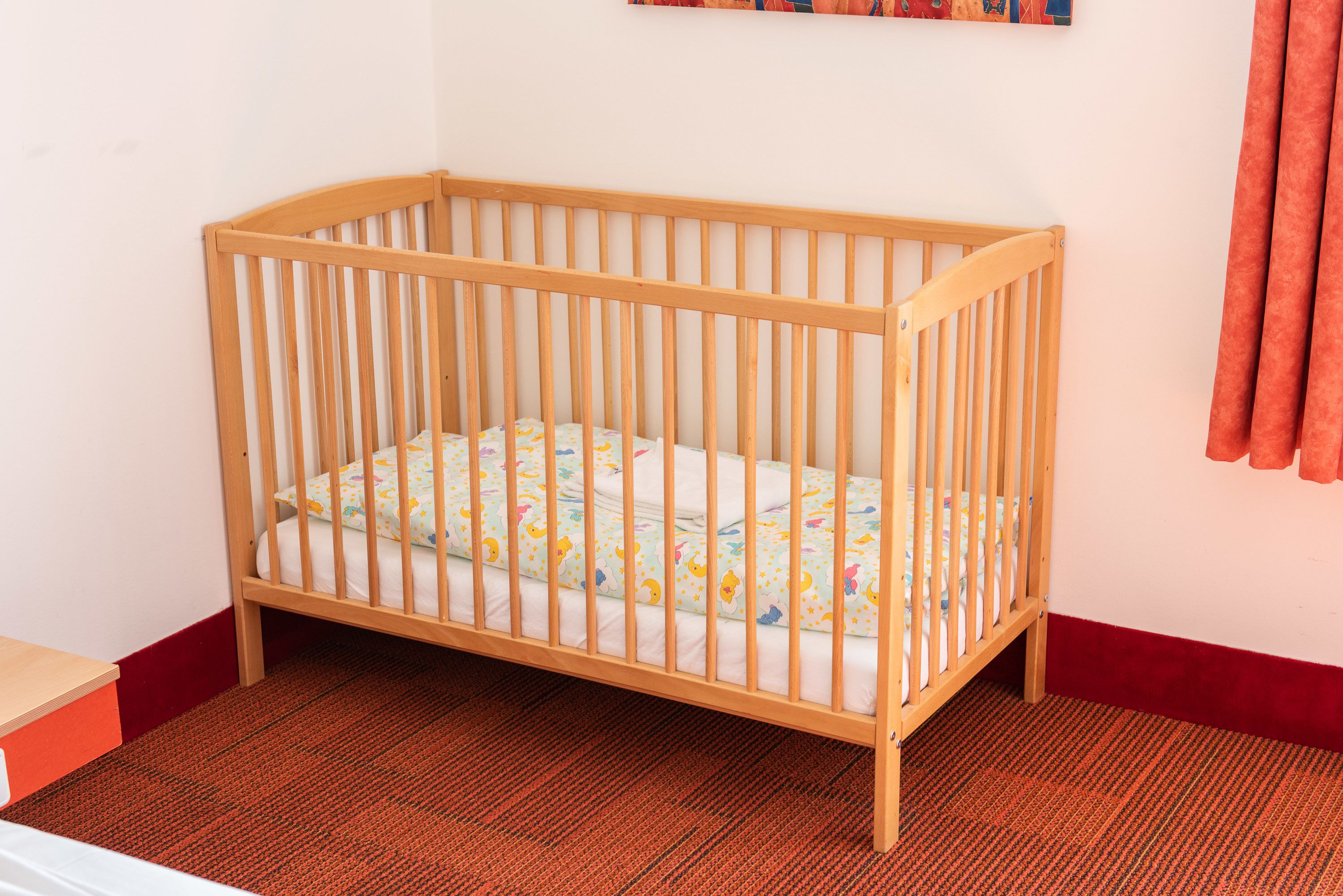 Een houten ledikant met een matras met dessin in een kamer met een rood tapijt en witte muren.