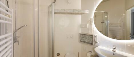 A bathroom with a glass shower enclosure, a toilet, a sink, and a mirror.
