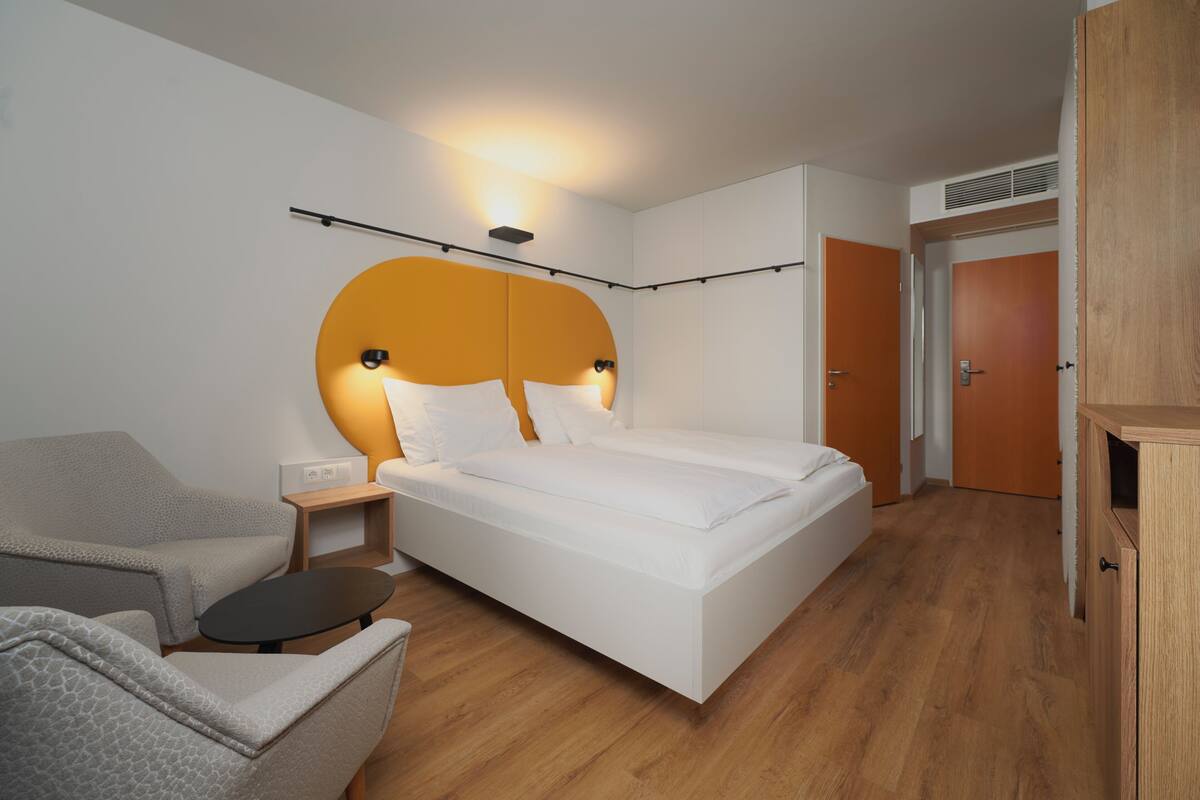 Een moderne hotelkamer met een bed, een bank, een kleine tafel en een kledingkast.
