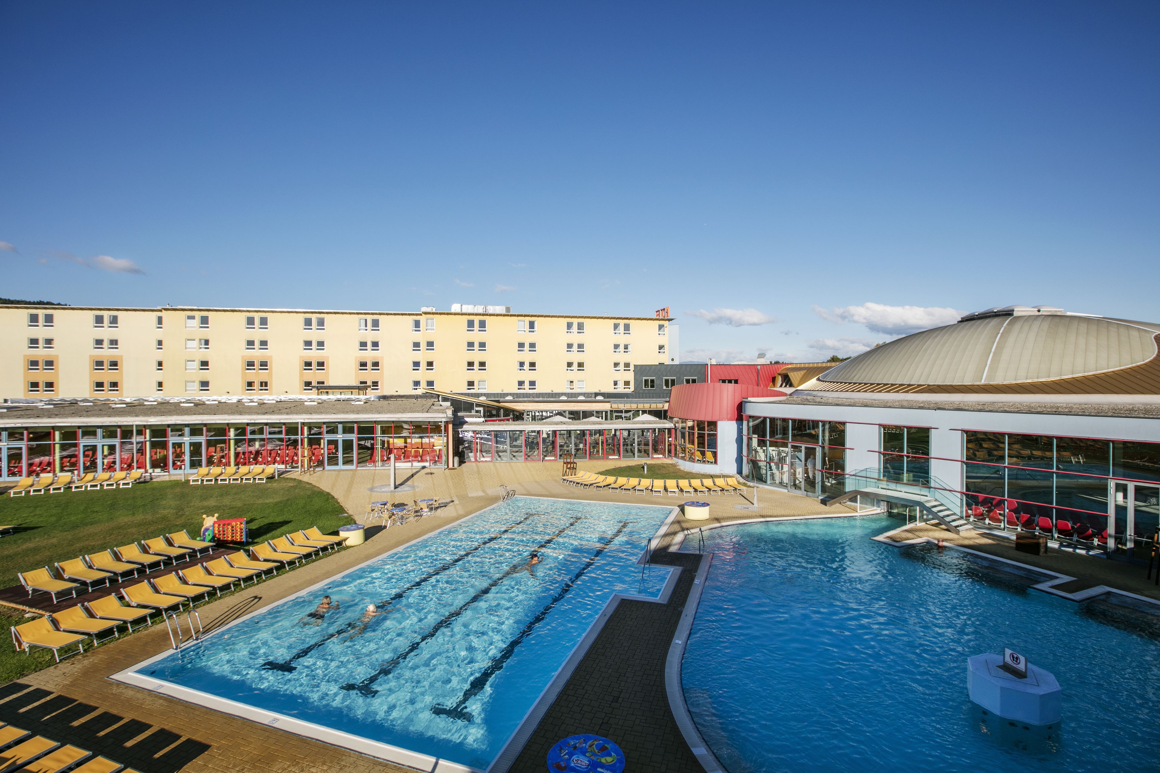 Ein Hotel mit einem großen Schwimmbad, Liegestühlen und einem überdachten Bereich.