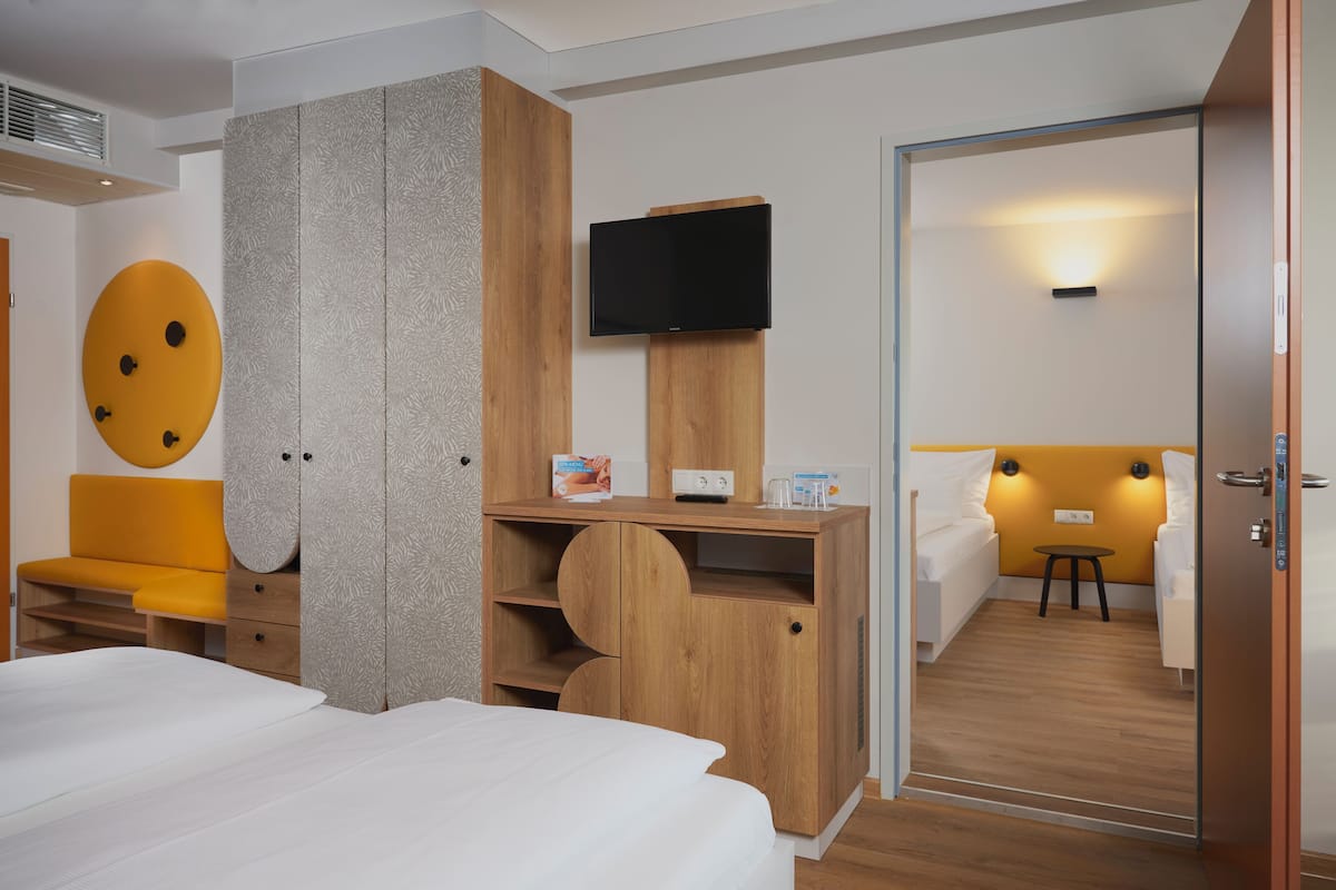 Een moderne hotelkamer met een bed, een houten garderobe, een televisie en een klein tafeltje.