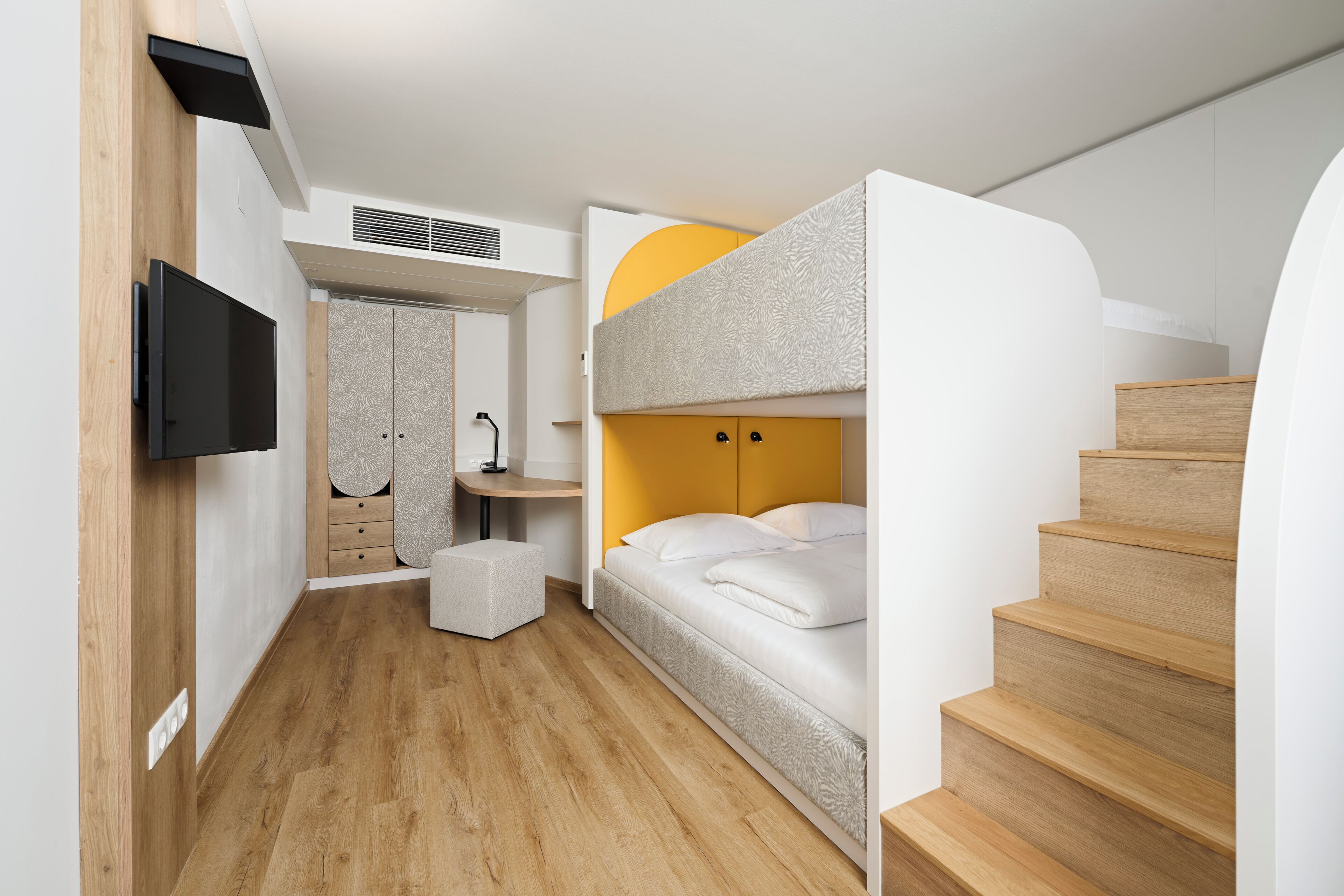 A compact room with a bunk bed, a desk, a chair, a television, and a staircase.