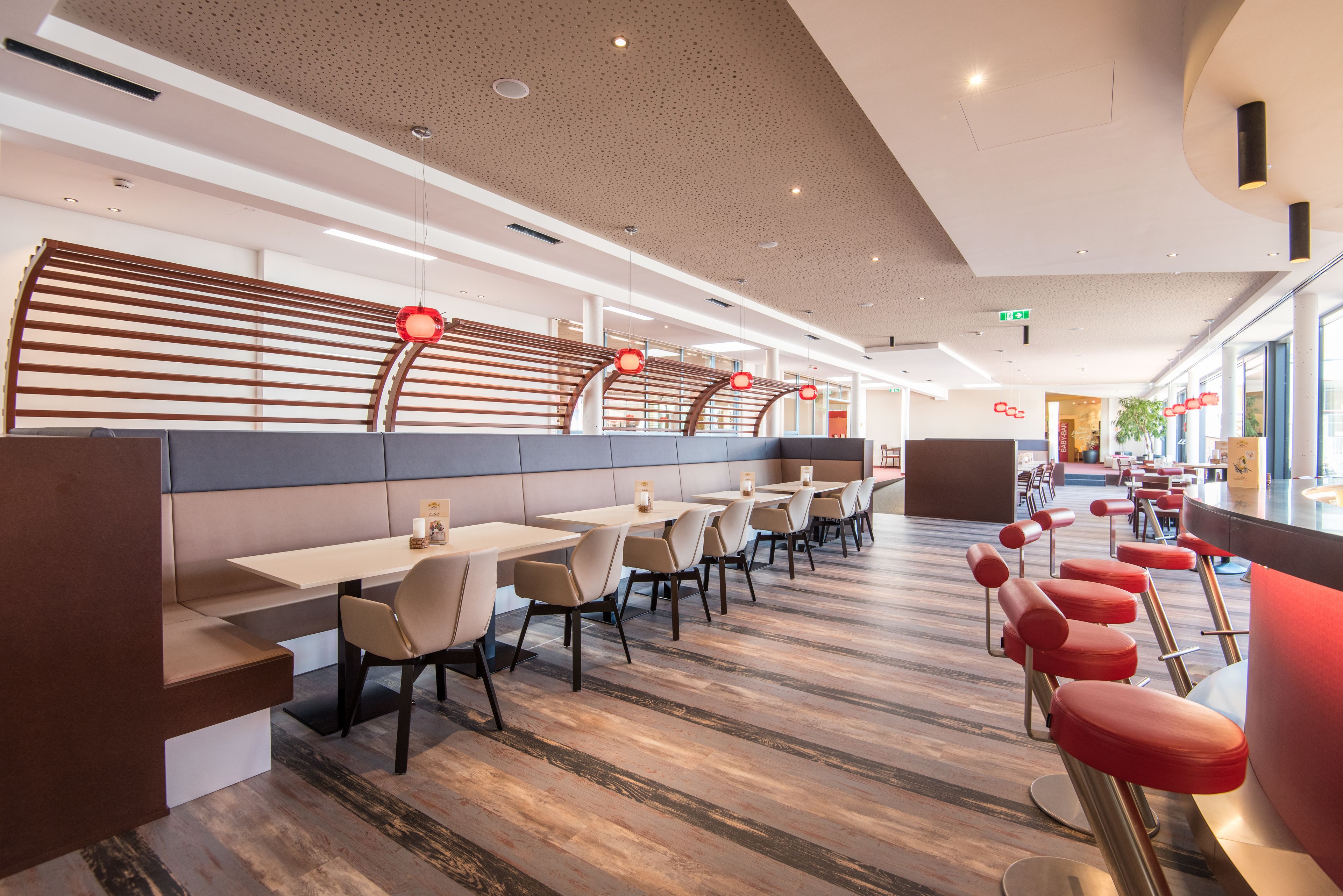 En moderne restaurant med lange fællesspisestole, polstrede boder og røde barstole.
