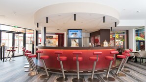 Un espace bar moderne avec un comptoir incurvé, de nombreux tabourets de bar rouges et un écran de télévision placé au-dessus du bar.