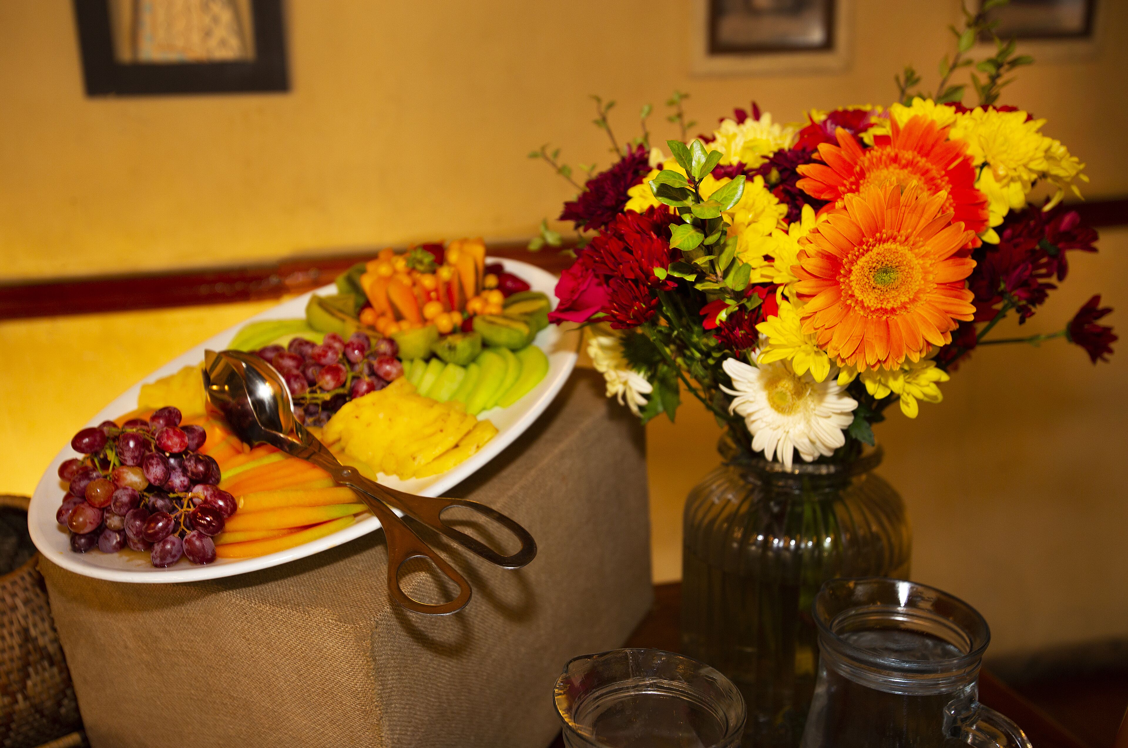 Une table avec une assiette de fruits, un vase de fleurs et une paire de ciseaux.