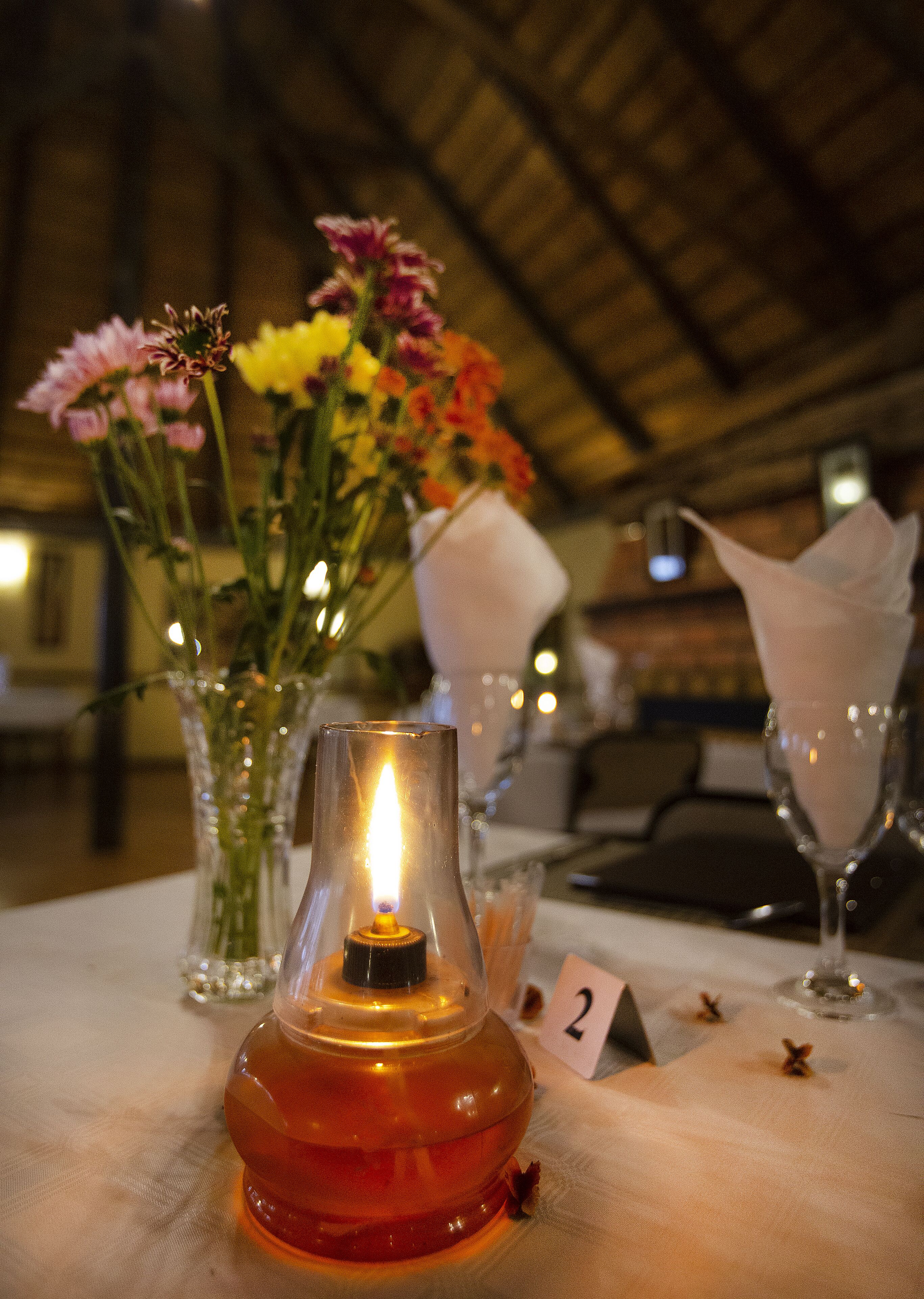Una mesa con una vela encendida, un florero con flores y una tarjeta con un número.