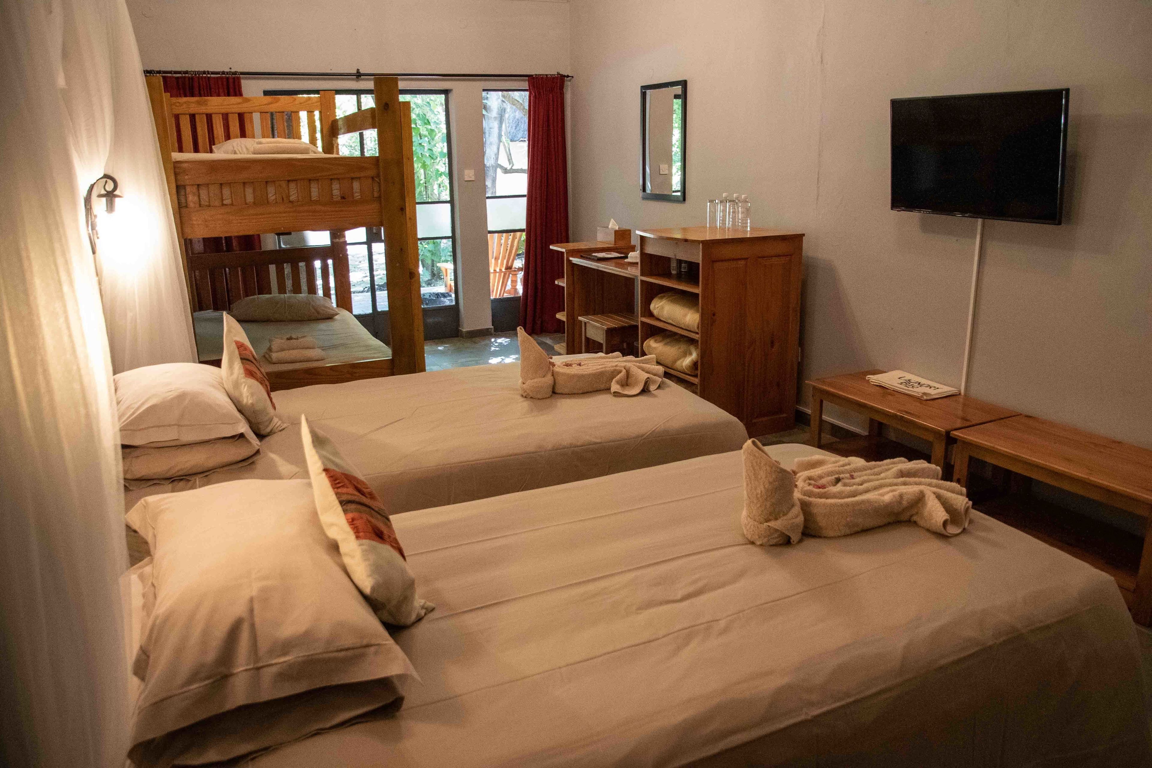 A room with two beds, a wooden bunk bed, a TV, a wooden cabinet, and a bench.
