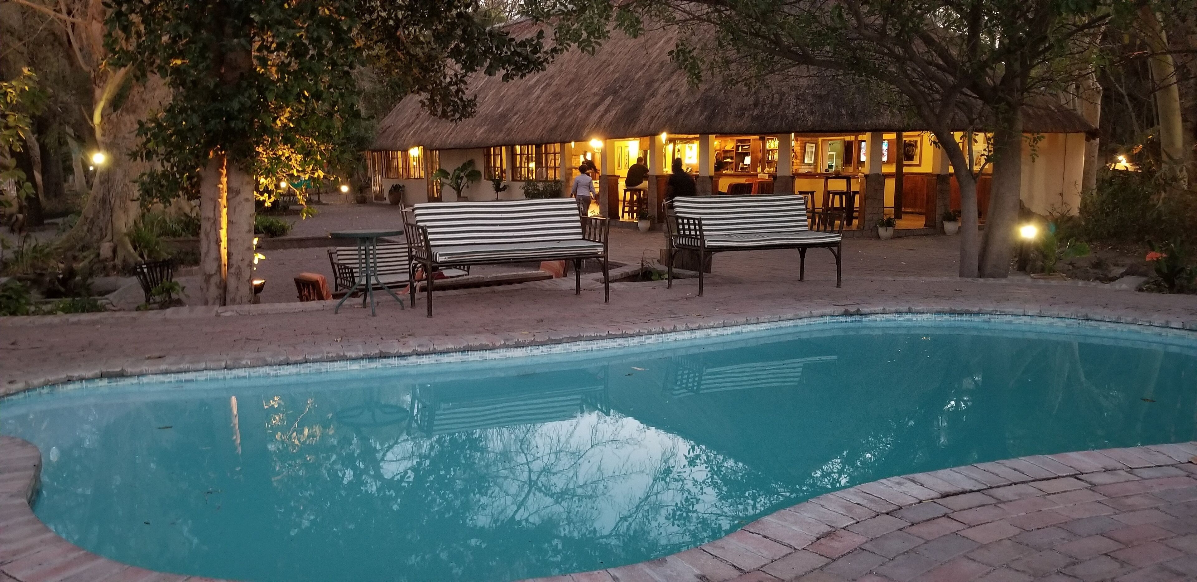 A pool area with benches and a thatched-roof building in the background.