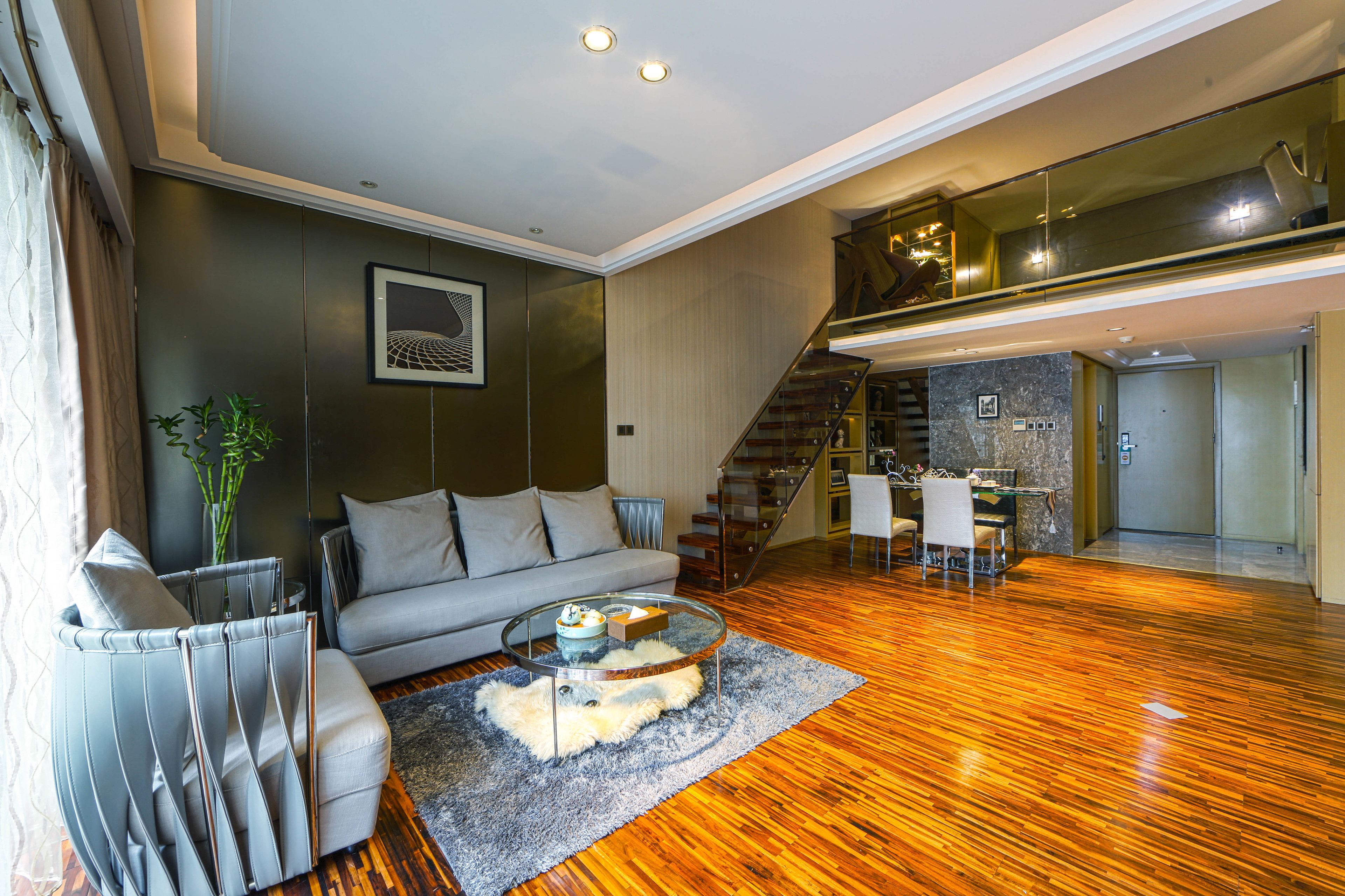 A modern living room with a grey sofa, a glass coffee table, and a wooden floor.