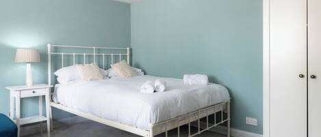 A bedroom with a white metal bed frame, a bedside table with a lamp, and a wardrobe.