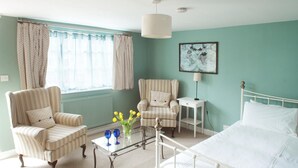 A room with a bed, two striped armchairs, a small table with a vase of flowers, a lamp, and a framed picture on the wall. - The Lodge (Corsham)