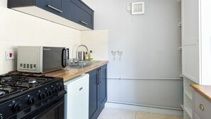 A compact kitchen with a gas stove, a microwave, and a small refrigerator. There is a wooden countertop, a sink with a faucet, and a wall-mounted exhaust fan. - The Lodge (Corsham)
