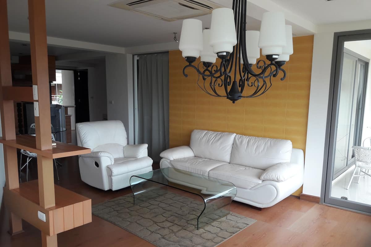 A modern living room with a white sofa, a glass coffee table, and a wooden TV stand.