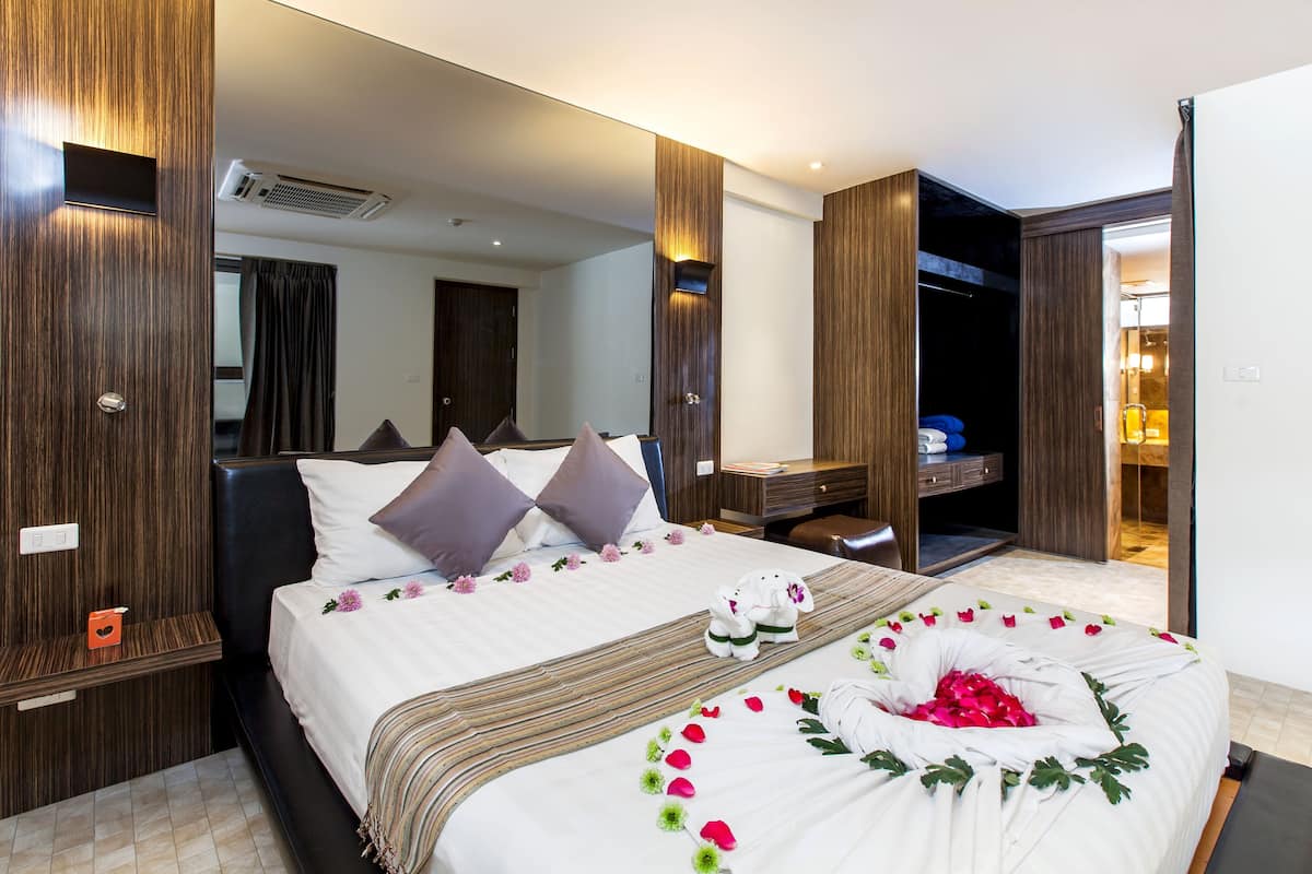 A hotel room with a large bed, a desk, a wardrobe, and a mirror.