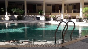 Piscina con escalones de acceso, rodeada de sillones de descanso y plantas en macetas.