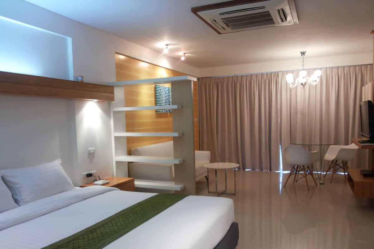 A modern hotel room with a large bed, a desk, a chair, a television, and a window with curtains.