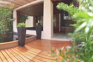 A modern outdoor area with a wooden deck, potted plants, and a water feature. - The Green Golf Residence Condominium (Kathu)