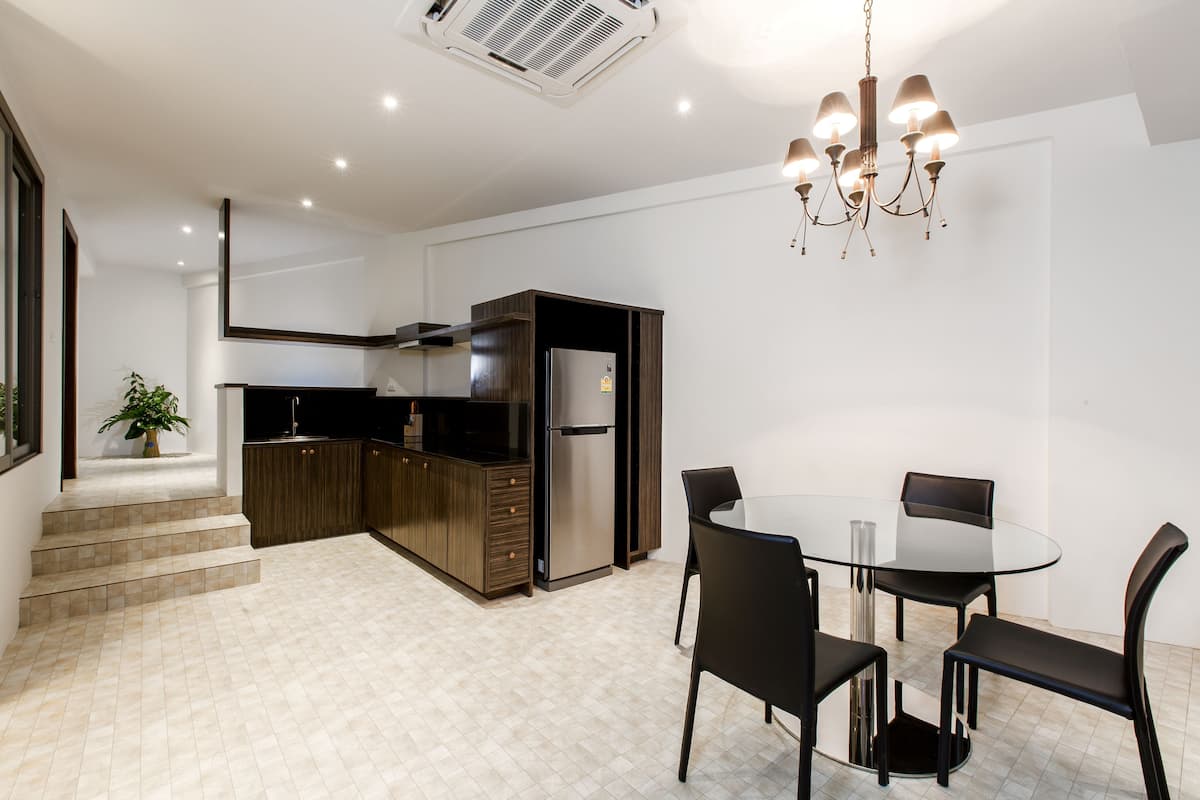 A modern kitchen with dark wooden cabinets, a stainless steel refrigerator, and a glass dining table with four chairs.