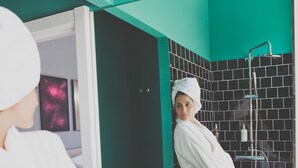 Una persona con bata blanca sentada en un baño con paredes de azulejos negros y una pared de acento verde.