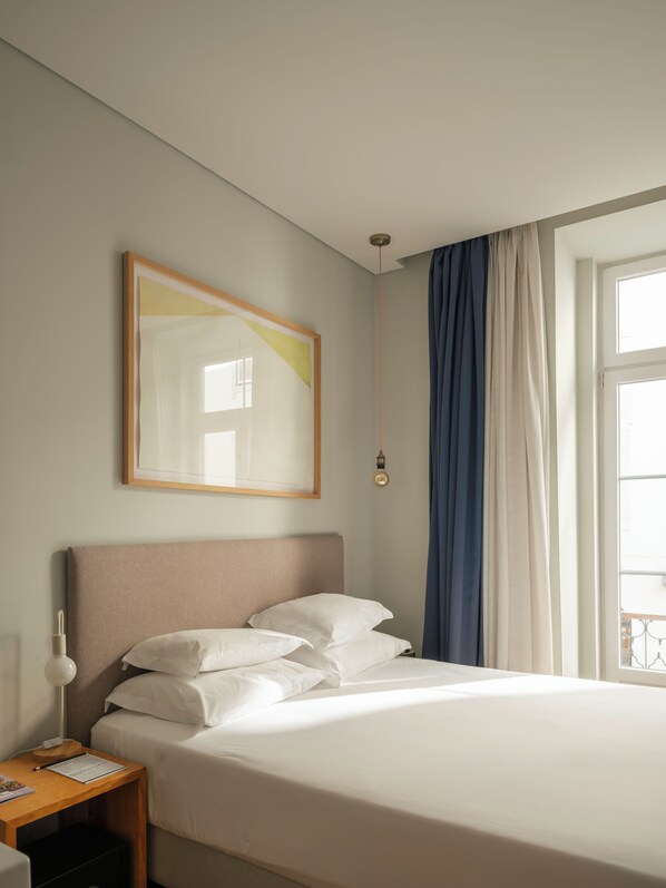 Een hotelkamer met een bed, nachtkastje met lamp, een lijst met foto aan de muur en een raam met gordijnen.