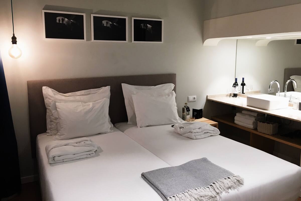 Hotellihuone, jossa on sänky, yöpöytä lampun kanssa, peili ja kolme kehystettyä kuvaa seinällä.