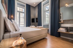 A modern hotel room with a large bed, a bedside table with a lamp, a mirror, and a window with curtains. - Esqina Urban Lodge (Lisbon)