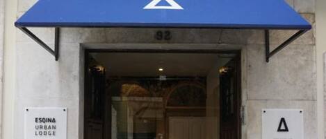 L’entrée d’un immeuble avec un auvent bleu et une enseigne indiquant qu’il s’agit de l’Esquina Urban Lodge.