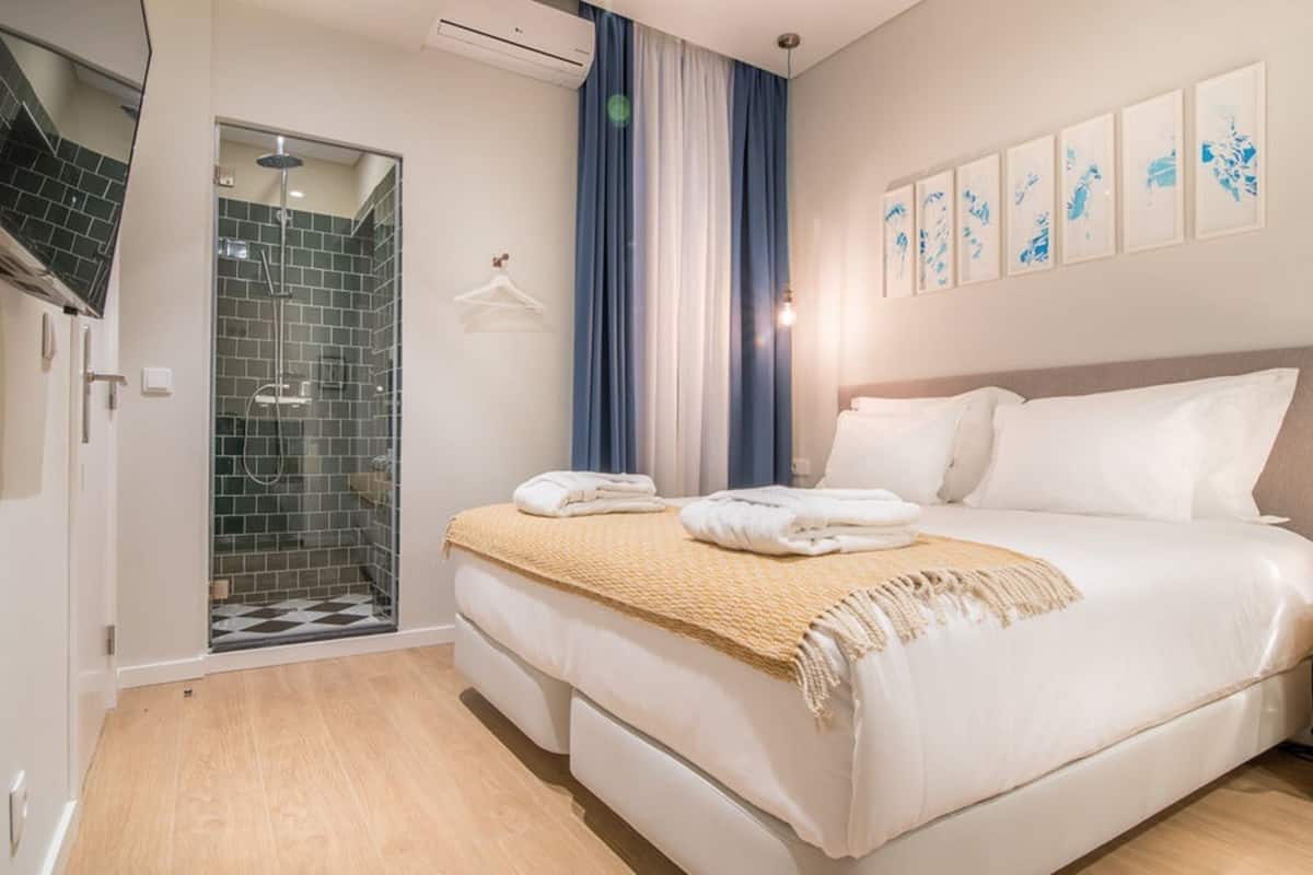 Hotellihuone, jossa on sänky, suihku ja seinälle asennettu televisio.