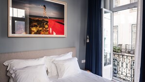 Habitación de hotel con cama, una obra de arte enmarcada en la pared y vista al balcón exterior.