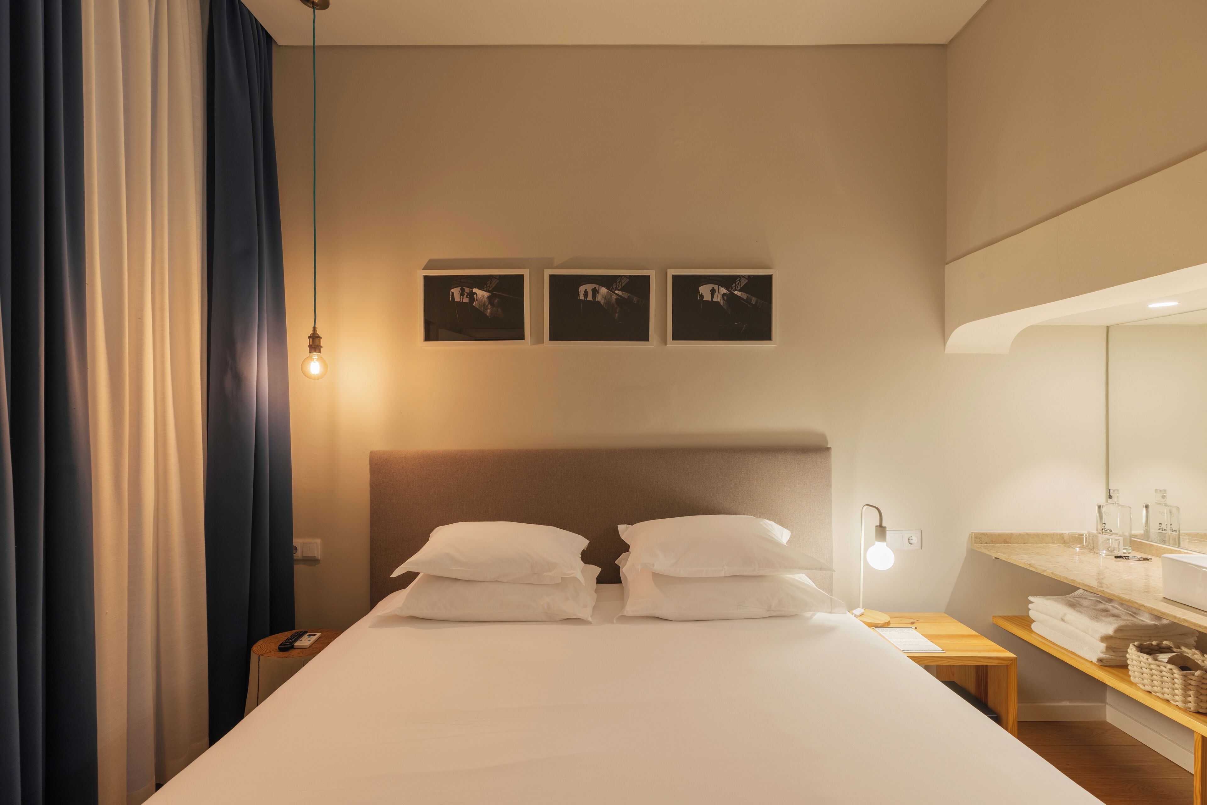 Ein Hotelzimmer mit Bett, Nachttisch, Lampe und Wandbildern.