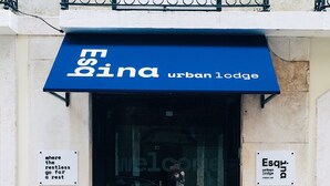 Entrada a un hostal urbano con un toldo azul, un coche estacionado adentro y dos letreros en las paredes.