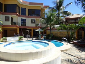 Un área de piscina con jacuzzi, sillas de descanso y palmeras.