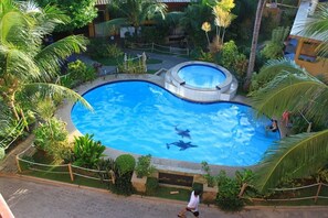 Una piscina rodeada de vegetación exuberante y palmeras, con un delfín visible en el agua.