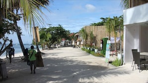 Un paseo marítimo con palmeras, una estructura de techo de paja y un restaurante con terraza.