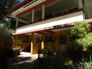 Un edificio de dos pisos con balcón, paredes de piedra y plantas en macetas.