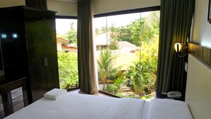 Habitación de hotel con una cama grande, un armario, teléfono en la mesita de noche y vistas a un jardín y edificios.