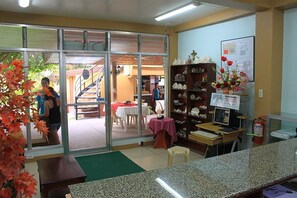 Una zona de recepción con mostrador, computadora, extintor y un arreglo floral.