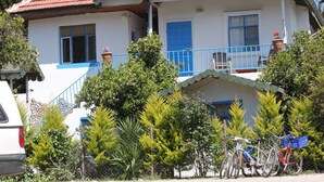 A two-story house with a balcony, surrounded by greenery and parked bicycles. - Harun Mila Pension (Kemer)