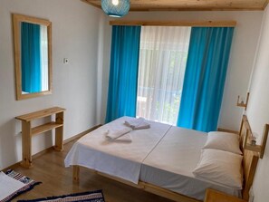 A room with a bed, a wooden headboard, a bedside table, and a window with curtains. - Harun Mila Pension (Kemer)