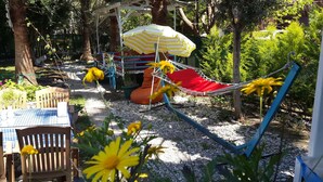 A garden with a hammock, a striped umbrella, and a table with chairs. - Harun Mila Pension (Kemer)