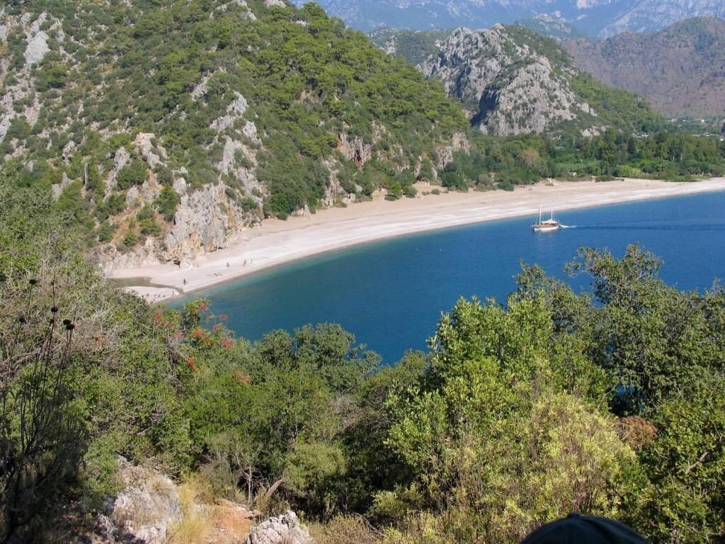 Un paisaje costero con playa, colinas rocosas y abundante vegetación.