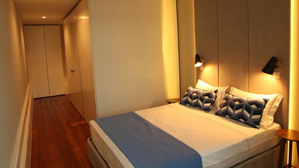 A modern bedroom with a large bed, a wardrobe, and a nightstand with a lamp.