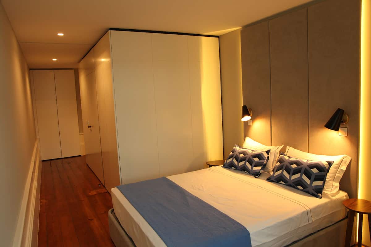 A modern bedroom with a large bed, a wardrobe, and a nightstand with a lamp.
