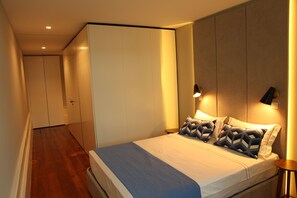 A modern bedroom with a large bed, a wardrobe, and a nightstand with a lamp. - New Oporto Apartments - Mouzinho (Porto)