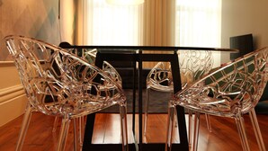 A dining area with a glass table and chairs, a black sofa, and a large window with curtains.