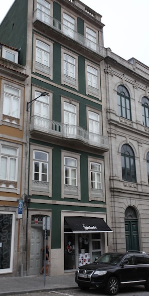 Um edifício de vários andares com fachada verde, janelas emolduradas a branco e varandas com grades de metal.