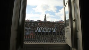 A view through a window with a decorative metal grille, overlooking a building with a tower and other structures.