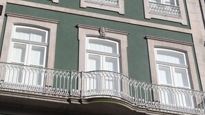 A multi-story building with a green facade, white-framed windows, and ornate balcony railings.