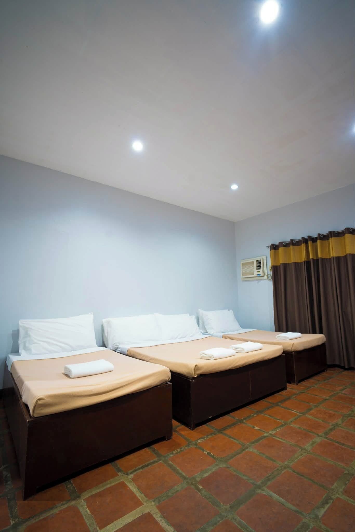 Habitación de hotel con dos camas, una ventana con cortinas, aire acondicionado de pared y piso de baldosas.