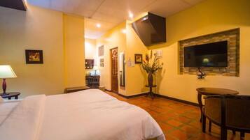 Una habitación de hotel con una cama, televisión montada en la pared, una mesita y una silla.